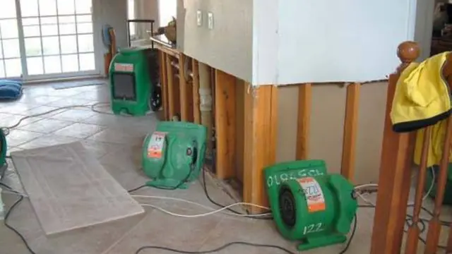 Green air movers and dehumidifiers drying a room where wet drywall has been cut out to the studs