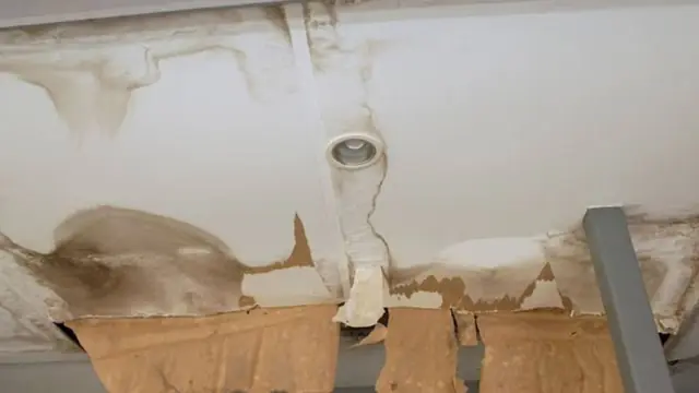 Water-stained ceiling around a light fixture with peeling paint and sagging drywall