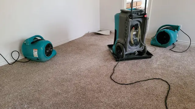 Two air movers and a dehumidifier drying a wet carpet in an empty room